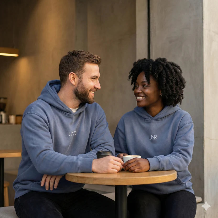 Two models wearing Denim UNR Pressure Hoodies with tonal chest logos at a café